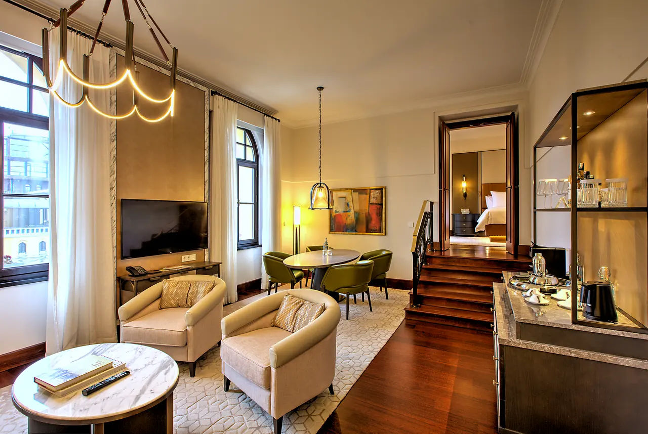 Four Seasons Hotels & Resorts — Süit salonu: koltuklar, yemek masası ve kemerli pencereler