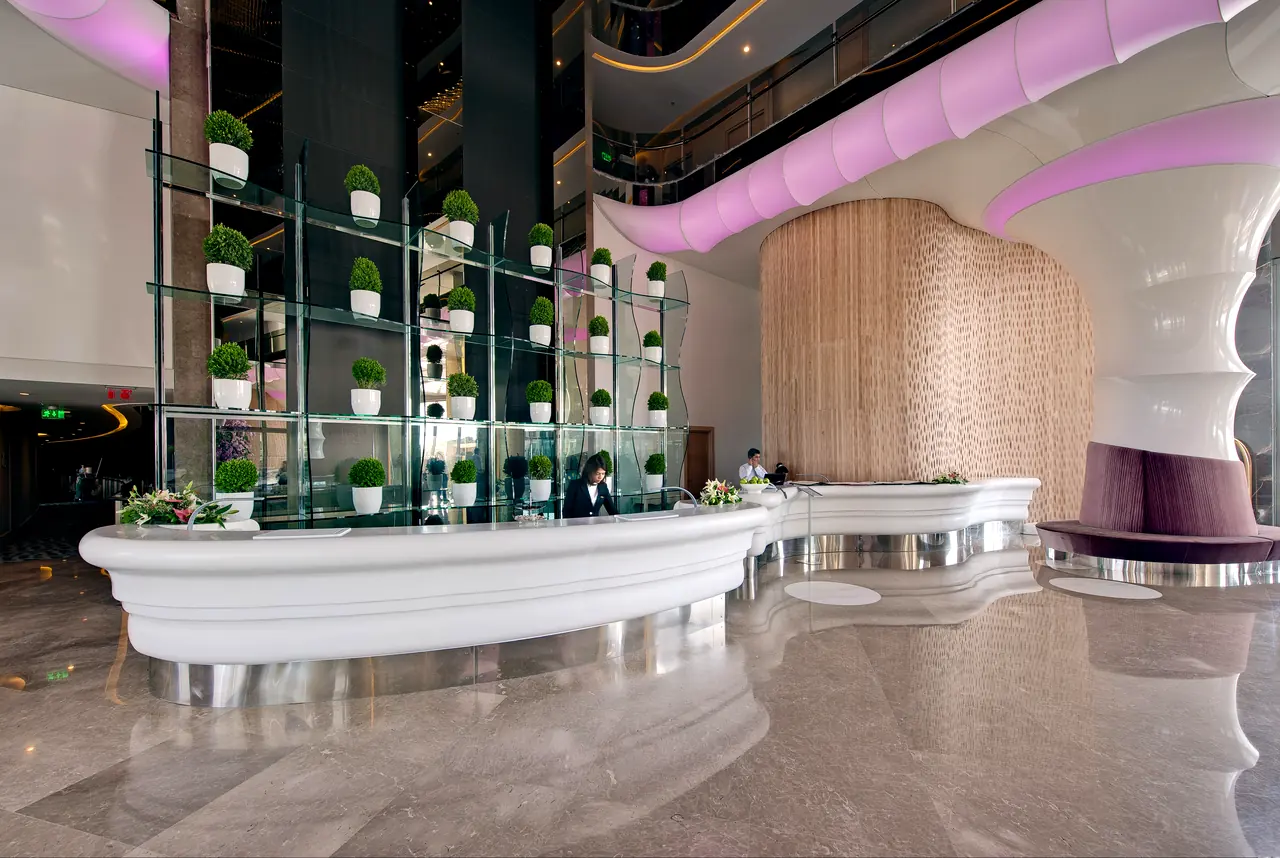 Maxx Royal Belek — Resepsiyon: beyaz kıvrımlı banko ve bitkili raflar