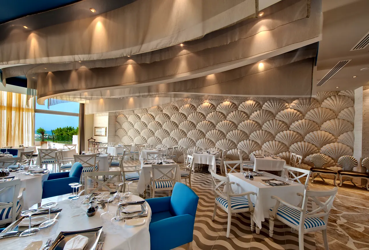 Maxx Royal Belek — Restoran: yelpaze desenli duvar ve mavi koltuklar